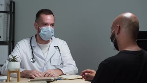 Un médecin brutal portant une blouse médicale et un masque de protection montre des pilules à son patient de sexe masculin