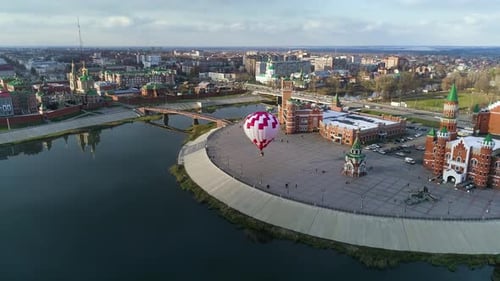 Coloured balloon flies over city embankment. People are walking around square