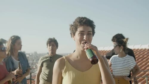 Happy Woman Drinking Beer From Glass Bottle at Rooftop Party