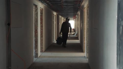 Person Walks Hallway Under Construction Carrying Bag