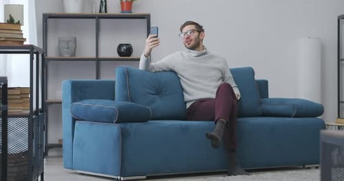 Man Video Chats on Smartphone from Home Couch