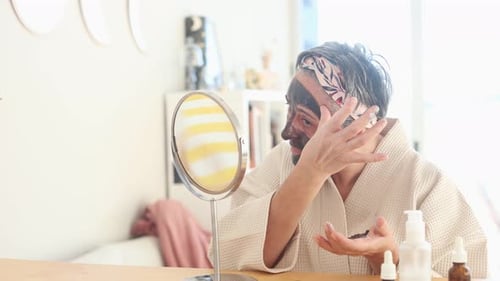 Woman Applying Facial Mask Looking at Mirror