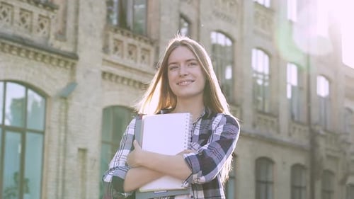 Garota estudante feliz em pé perto da faculdade. Segurando livros didáticos, sorrindo