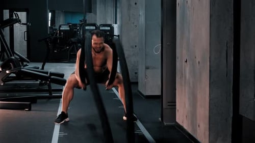 Muscular Man Exercising with Battle Ropes in Gym