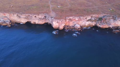 Top down aerial view of waves splash against rocky seashore, background. Flight over high cliffs of
