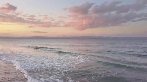 Aerial view of a sea surface with blue water waves under sunset sky.