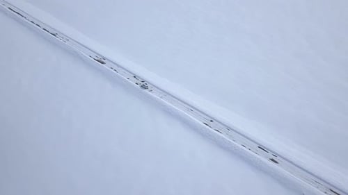 Aerial View on Car Driving Through Winter Forest Road Between the Snowcovered Fields