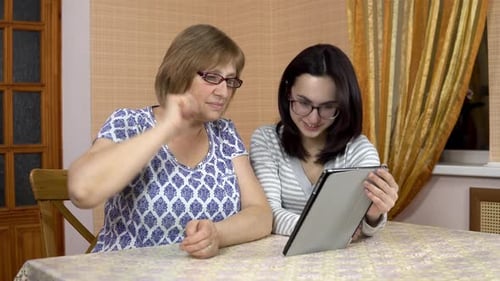 Daughter Teaches Mother How To Use a Tablet. A Young Woman Shows Her Old Mother Where To Click on a