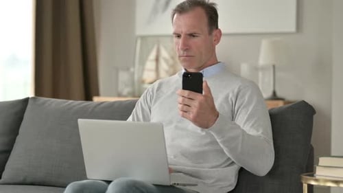 Man Using Phone and Laptop Indoors