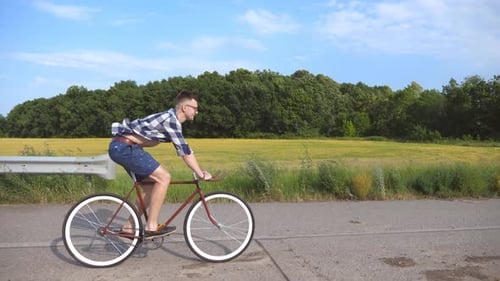 Junger gutaussehender Mann reitet auf einem Oldtimer-Fahrrad auf der Landstraße. Sportlicher Typ beim Radfahren auf der Strecke