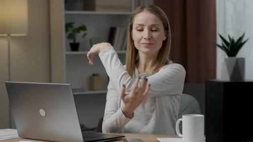 Ambitious smiling young woman sitting in the office space and stretching her arms after hardworking