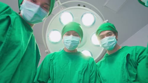 Asian professional medical team performing surgical operation in modern operating room in hospital.