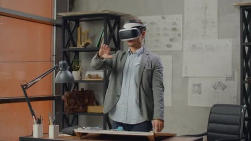 Male Engineer in the Office in a Virtual Reality Helmet Uses Gestures to Manage the Project Without
