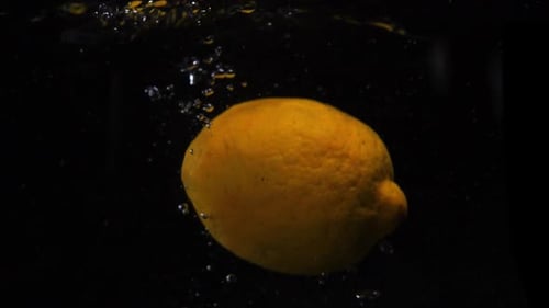 Yellow Lemon Falls Into Water on Black Background. Slow Motion Macro Shot. Food Video Lemon