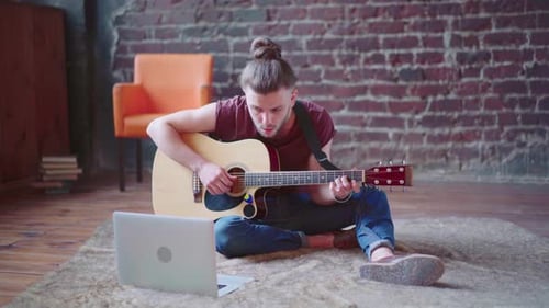Young Man Plays Guitar at Home with Laptop