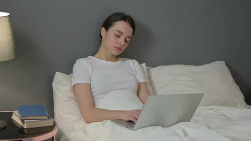 Drowsy Woman with Laptop Falling Asleep in Bed