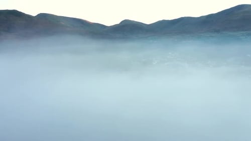 Aerial view of a lake and town covered by fog and clouds at sunset