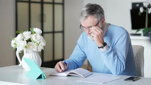 Man Writing in Notebook at Table Indoors