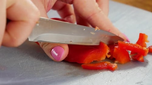 Female is cutting red bell pepper in home kitchen, close up view