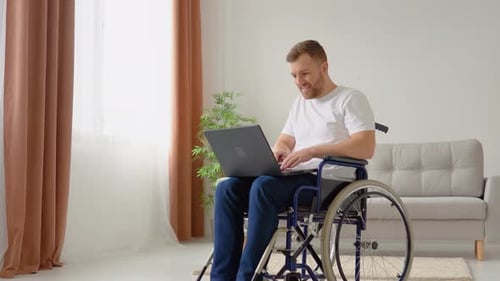 Man in Wheelchair Using Laptop Inside Bright Room