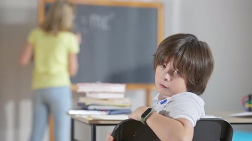 Boy Sits at School Desk with Chalkboard
