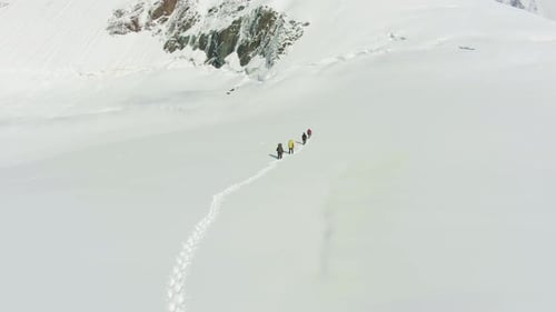Eine Gruppe von Bergsteigern wird in verschneiten Bergen zusammengeseilt. Luftbild