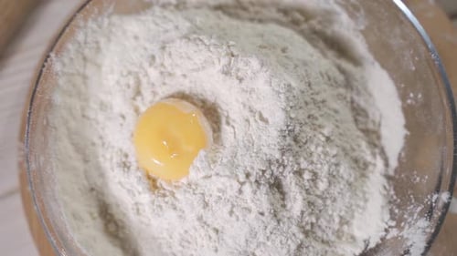 Egg Yolk Dropping Into Flour in Glass Bowl