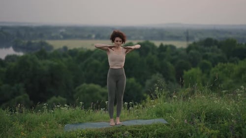 A Young Woman Does Yoga Exercises Standing on the Top of a Forest Mountain Against the Background of