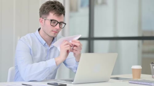 Young Man Folds Paper Airplane at Desk
