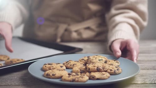 Hausgemachte Schokoladenkekse auf mit Backblech ausgelegtem Backblech. Mädchen in einem Pullover legt Kekse auf eine weiße Platte