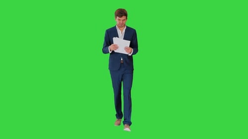 Serious Businessman Reading Documents or Report While Walking on a Green Screen, Chroma Key.