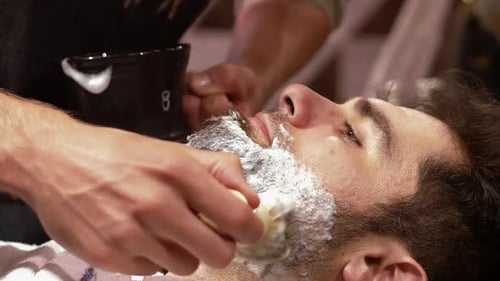 Mann lässt sich im Friseurladen mit Rasierpinsel rasieren