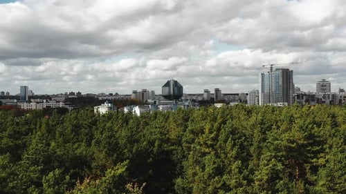 Drone Flying Above Green Trees and Autumn Suburb Neighborhood Towards Urban Panorama of Minsk Near