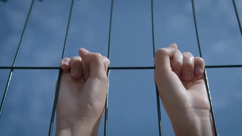 Close Up of Hands Gripping Metal Fence