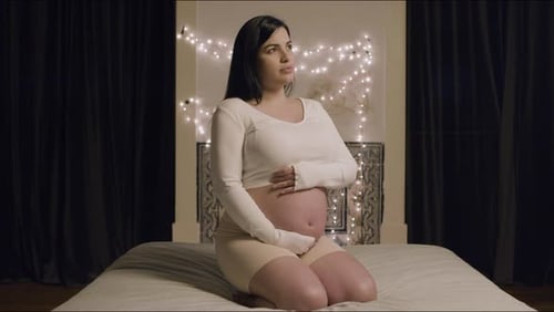Cheerful Pregnant Woman Sitting on Bed and Stroking Belly