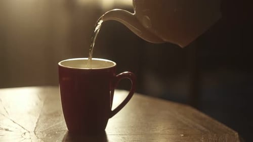 The Teapot Pours Hot Tea Into a Cup in the Golden Rays of the Sun