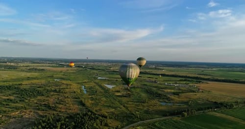 Beautiful aerostats in the air. Several colorful hot air balloons flying over green fields. Aeronaut