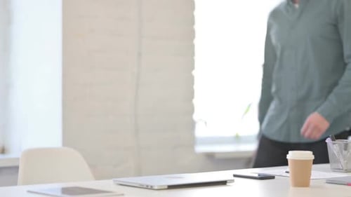 Man Opens Laptop at Desk in Bright Office