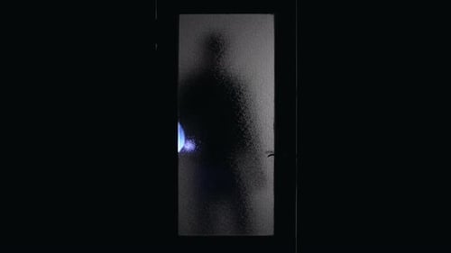 Menacing Shadow Figure with Flashlight Behind Frosted Glass