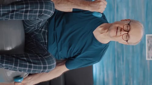 Senior Man Lifts Weights on Fitness Ball at Home