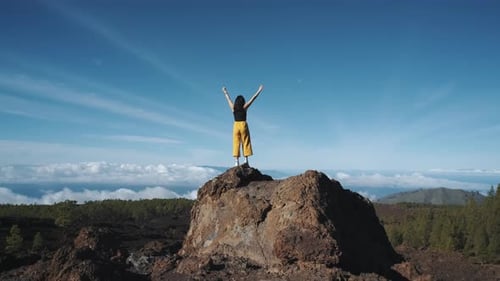 Woman Stands on Mountain Top with Arms Raised