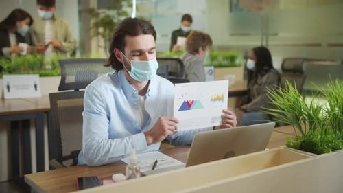Masked Man Reviews Charts at Modern Office Workplace