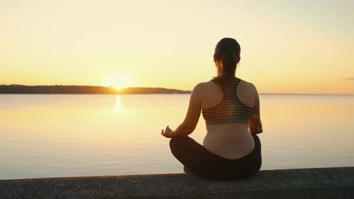 The Girl Meditates in the Lotus Position on the Lake at Sunset