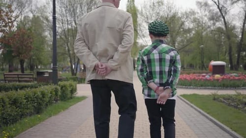 Portrait Grandfather and Grandson Walking in the Park with Their Backs To Camera