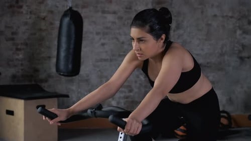 Portrait adult Indian woman training on static bike at cycling class. Fitness woman spinning bike