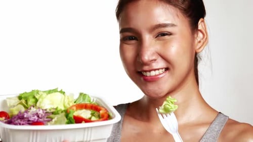 Garota sorridente em roupas esportivas segurando uma tigela de salada sobre fundo branco
