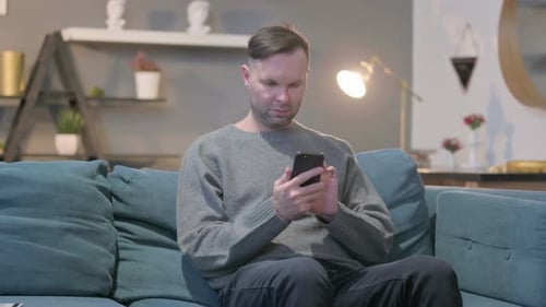 Man Using Smartphone on Teal Couch at Home