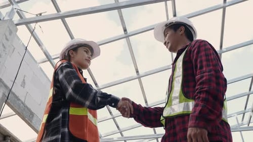 engineer worker woman & man in protective helmet and uniform shaking hands