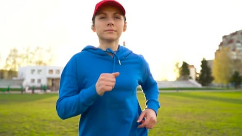Woman with Wireless Headphones Runs Through the Stadium at Sunset