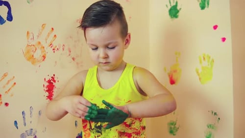 Close Up of Little Cute Child with Painted in Green Hands Making Colorful Handprints on the Wall